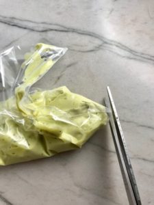 Scissors cutting tip off baggie filled with avocado crema. Roasted Carrots with smoky cumin and scallions, then topped with Avocado Crema are such a delicious and quick side dish for dinner. Roasting brings out the natural sugar in the carrots, so they get a sweet caramelization with the salty and smoky flavors. The Avocado crema gives creamy and silky balance.