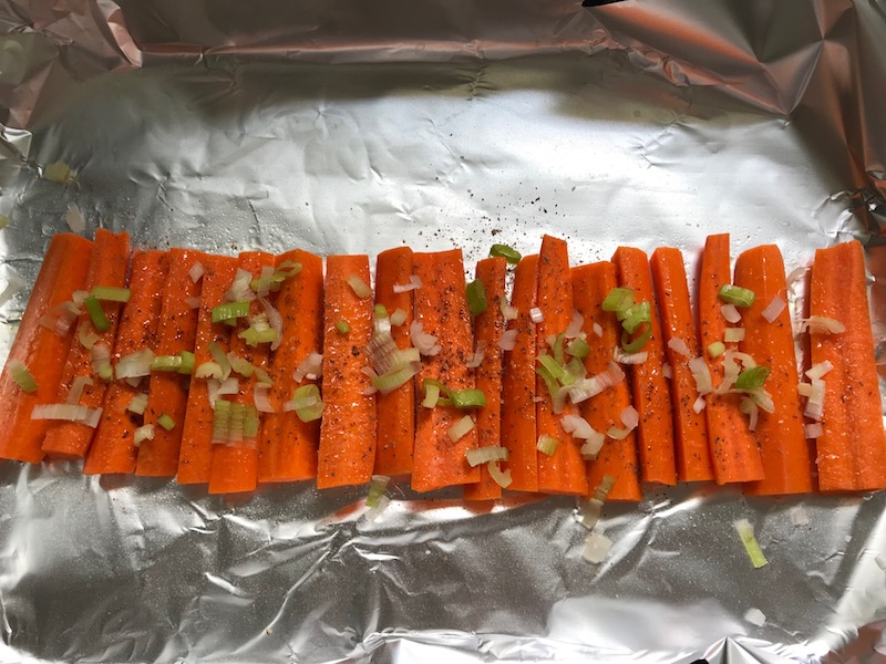 Raw carrots lined up on pan seasoned with sliced scallions over top. Roasted Carrots with smoky cumin and scallions, then topped with Avocado Crema are such a delicious and quick side dish for dinner. Roasting brings out the natural sugar in the carrots, so they get a sweet caramelization with the salty and smoky flavors. The Avocado crema gives creamy and silky balance.