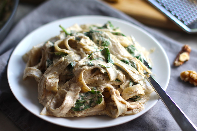 Close up of Walnut Sauce recipe with Ricotta and Spinach mixed with Fettuccine on a white plate with fork. The recipe is thick, rich, nutty, and creamy. It's inspired by the traditional Italian Walnut Sauce from the North-Western Italy, Liguria Region, but my Walnut Sauce recipe adds even more decadence with creamy ricotta and more nutty parmesan cheese.