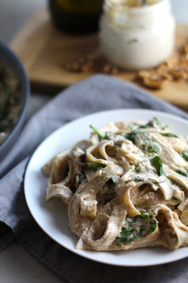 This Walnut Cream Sauce recipe with Ricotta and Spinach on a white plate on napkin with walnuts and jar in background. This recipe is thick, rich, nutty, and creamy.  It's inspired by the traditional Italian Walnut Sauce from the North-Western Italy, Liguria Region, but my Walnut Sauce recipe adds even more decadence with creamy ricotta and more nutty parmesan cheese.