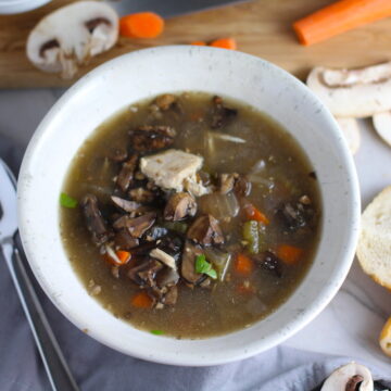 Chicken and Mushroom Soup in white bowl with raw mushrooms, carrots, wood cutting board, bread, and spoon on counter. This Slow Cooker Chicken and Mushroom Soup is warm, hearty, comforting, earthy, and just devine. The mix of blended and chunky mushrooms with carrots, onions, celery, shredded chicken, and herbs gives you a perfect bite every time.