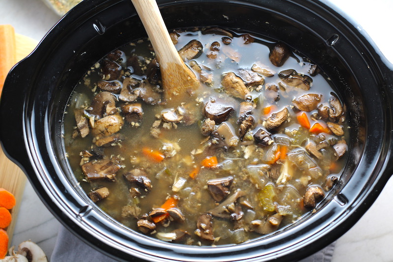 Cooked chicken and mushroom soup in slow cooker with wood spoon. This Slow Cooker Chicken and Mushroom Soup is warm, hearty, comforting, earthy, and just devine. The mix of blended and chunky mushrooms with carrots, onions, celery, shredded chicken, and herbs gives you a perfect bite every time.