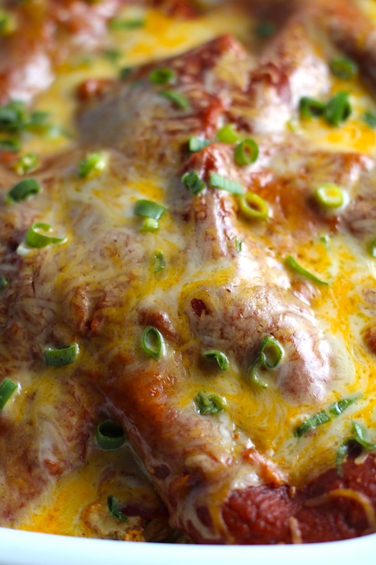 Extreme close up picture of cheesy top of Ground Chicken Taco Casserole with red sauce topped with melted cheese and scallion slices.