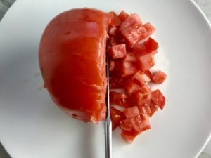 Tomato being diced on cutting board. This Creamy Mexican Pasta Salad has Sun Dried Tomatoes, Corn, Fresh Diced Tomatoes, Cilantro, and smoky Mexican spices. The dressing is creamy and smoky with lots of depth and a hint of sweetness from the Sun Dried Tomatoes that are blended in. Terrific as a side or mix in some chicken or beef and call it a meal!