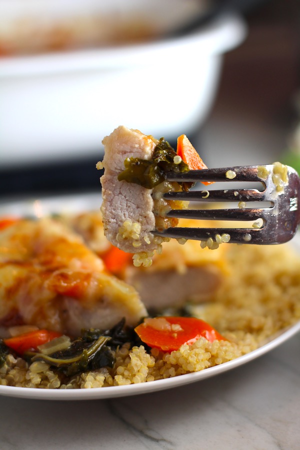 Close up of Smothered Pork Chop bite on a fork held over plate. This Smothered Pork Chops with Vegetables recipe is a true midwestern comfort dish with layers of vegetables and meaty pork chops smothered in a creamy sauce and cheese. The pork chops in this delicious casserole are left whole so that you get an entire portion dripping in goodness in one scoop.