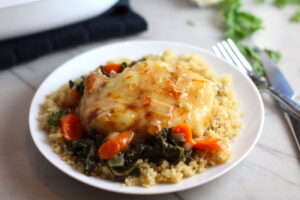Pork Chop with cheese melted on top over carrots and kale on top of quinoa on plate on counter with casserole dish in background. Smothered Pork Chop Casserole is a true midwestern comfort dish with layers of vegetables and meaty pork chops smothered in a creamy sauce and cheese. The pork chops in this delicious casserole are left whole so that you get an entire portion dripping in goodness in one scoop.