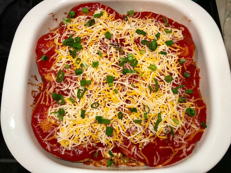 Casserole Dish with the start of the Chicken Taco Casserole Recipe being assembled. Tortillas and ground meat, black beans, tomatoes, and scallions on top.