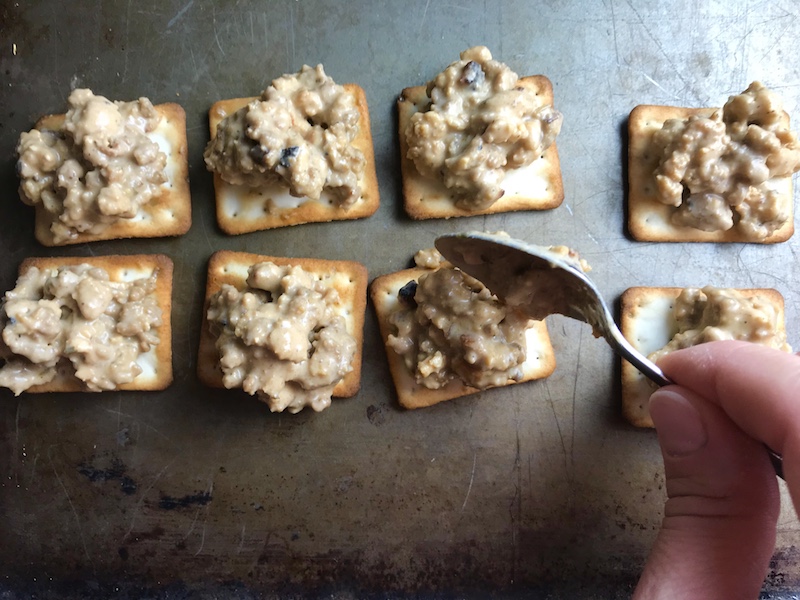 Adding Hanky Panky Meat topping to GF crackers on sheet pan. These Hanky Panky Canapes are the BEST Party Appetizers around! They cheesy, meaty, and absolutely delicious. Ground Beef is mixed with Homemade Chicken Sausage and then combined with lots of cheese until its a creamy addictive pot of goodness. Then it is scooped on top of bread, toasts, or crackers