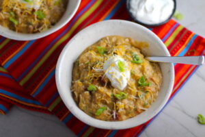 2 Bowls of Chipotle Chicken Enchilada Stew on red napkin with sour cream and scallion slices as garnish. It's one of my Prepped Freezer Meal recipes and it's creamy, cozy, hearty, cheesy, and slightly spicy. All ingredients freeze raw, thaw, then cook in the slow cooker or in the oven. It's a stew because it's thick and hearty with bites of chicken, carrots, onion, chipotle peppers, cumin, garlic and tortilla chips that melt down to thicken this delicious stew.