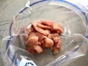 Cut chicken in freezer bag for Chipotle Chicken Enchilada Stew. It is one of my Prepped Freezer Meal recipes and it's creamy, cozy, hearty, cheesy, and slightly spicy. All ingredients freeze raw, thaw, then cook in the slow cooker or in the oven. It's a stew because it's thick and hearty with bites of chicken, carrots, onion, chipotle peppers, cumin, garlic and tortilla chips that melt down to thicken this delicious stew.