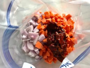 Chipotle peppers in adobo sauce added to freezer bag with chicken, carrots, and onions for Chipotle Chicken Enchilada Stew. It is one of my Prepped Freezer Meal recipes and it's creamy, cozy, hearty, cheesy, and slightly spicy. All ingredients freeze raw, thaw, then cook in the slow cooker or in the oven. It's a stew because it's thick and hearty with bites of chicken, carrots, onion, chipotle peppers, cumin, garlic and tortilla chips that melt down to thicken this delicious stew.