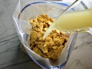 Chicken Broth pouring over crushed tortilla chips in a freezer bag for Chipotle Chicken Enchilada Stew. It is one of my Prepped Freezer Meal recipes and it's creamy, cozy, hearty, cheesy, and slightly spicy. All ingredients freeze raw, thaw, then cook in the slow cooker or in the oven. It's a stew because it's thick and hearty with bites of chicken, carrots, onion, chipotle peppers, cumin, garlic and tortilla chips that melt down to thicken this delicious stew.