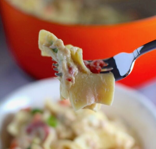 Cheesy Tuna Noodle Casserole Recipe bite on a fork over a bowl with pot in background. This is a creamy and delicious comfort dish with tuna and noodles and a surprise pop of sweet from Pimiento. This easy recipe is completely from scratch (no canned soup here!) but I can promise you it's so easy and only takes 30 minutes because it's a Casserole that you can make entirely on the stove top!