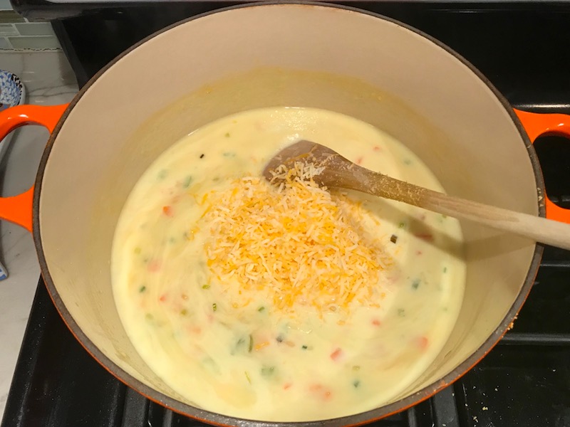 Spoon mixing shredded cheese into sauce in pot for Easy Tuna Casserole. This is a creamy and delicious comfort dish with tuna and noodles and a surprise pop of sweet from Pimiento. This easy recipe is completely from scratch (no canned soup here!) but I can promise you it's so easy and only takes 30 minutes because it's a Casserole that you can make entirely on the stove top!