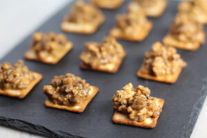 Cooked Hanky Panky on Black Slate Platter. These Hanky Panky Canapes are the BEST Party Appetizers around! They cheesy, meaty, and absolutely delicious. Ground Beef is mixed with Homemade Chicken Sausage and then combined with lots of cheese until its a creamy addictive pot of goodness. Then it is scooped on top of bread, toasts, or crackers