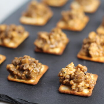 Cooked Hanky Panky on Black Slate Platter. These Hanky Panky Canapes are the BEST Party Appetizers around! They cheesy, meaty, and absolutely delicious. Ground Beef is mixed with Homemade Chicken Sausage and then combined with lots of cheese until its a creamy addictive pot of goodness. Then it is scooped on top of bread, toasts, or crackers