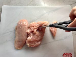 Cutting raw chicken with cooking scissors. This Freezer Hoisin Chicken with Red Peppers, Carrots, Onions, Ginger, and Soy sauce is delicious and so easy to make. You get sweet and savory all in one dish and it's perfect for kids because it's sweet, not spicy at all. Just freeze ahead, thaw, then cook on a sheet pan!