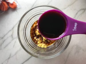 Adding soy sauce to ginger in small bowl on counter for Freezer Hoisin Chicken with Red Peppers, Carrots, Onions, Ginger, and Soy sauce is delicious and so easy to make. You get sweet and savory all in one dish and it's perfect for kids because it's sweet, not spicy at all. Just freeze ahead, thaw, then cook on a sheet pan!