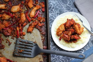 Hoisin Chicken over rice on a plate with a fork. To the left is pan with spatula. Freezer Hoisin Chicken with Red Peppers, Carrots, Onions, Ginger, and Soy sauce is delicious and so easy to make. You get sweet and savory all in one dish and it's perfect for kids because it's sweet, not spicy at all. Just freeze ahead, thaw, then cook on a sheet pan!