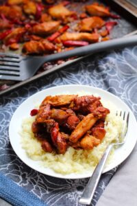Hoisin Chicken over rice on a plate with a fork. In back is pan with spatula. This Freezer Hoisin Chicken with Red Peppers, Carrots, Onions, Ginger, and Soy sauce is delicious and so easy to make. You get sweet and savory all in one dish and it's perfect for kids because it's sweet, not spicy at all. Just freeze ahead, thaw, then cook on a sheet pan!