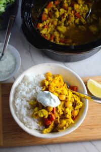 Moroccan Chicken Chili in bowl over white rice with a dollop of Cilantro Lime Yogurt on top and in a bowl to the left. The slow cooker is in background with chili. Moroccan Chicken Chili with Chickpeas is loaded with comforting and healthy ingredients and spices. You get warmth from Ginger, Turmeric, Garlic, and Coriander. Then tons of hearty flavor from browned ground chicken and Shallots. And creaminess from the Carrots and Chickpeas. You can make it ahead and freeze it until you are ready to cook it!