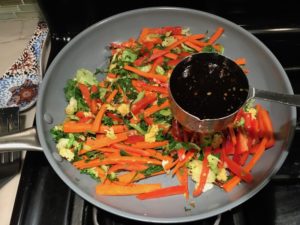 Adding Soy Sauce to stir fry veggies in pan for Asian Lettuce Wraps. They are a fantastic way to use leftover Turkey or Chicken transforming it with new delicious flavors and textures. The turkey is stir fried with carrots, red pepper, and brussel sprouts in a flavorful ginger, garlic, & sesame sauce. It's layered in lettuce wraps with rice and a cool, crunchy purple cabbage sesame slaw. Serve with a Garlic Honey Soy Sauce....YUM!!!