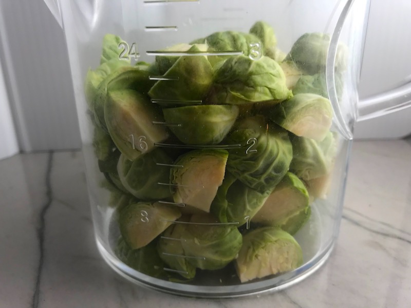 Cut raw Brussel Sprouts in measuring cup for the Easy Bacon Brussel Sprouts and Chicken recipe. It's a perfect quick Fall Recipe! It has a creamy sauce filled with salty bacon, earthy and almost nutty seared brussel sprouts, and hearty healthy chicken. Serve over rice (or Quinoa or pasta!).