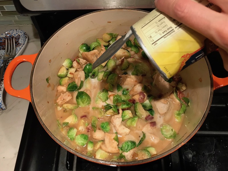 Adding Coconut Milk to brussel sprouts and chicken in pot for the Easy Bacon Brussel Sprouts and Chicken recipe. It's a perfect quick Fall Recipe! It has a creamy sauce filled with salty bacon, earthy and almost nutty seared brussel sprouts, and hearty healthy chicken. Serve over rice (or Quinoa or pasta!).
