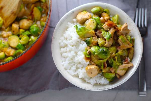 Easy Bacon Brussel Sprouts and Chicken served over white rice in a bowl with orange pot in background. It is a perfect quick Fall Recipe! It has a creamy sauce filled with salty bacon, earthy and almost nutty seared brussel sprouts, and hearty healthy chicken. Serve over rice (or Quinoa or pasta!).