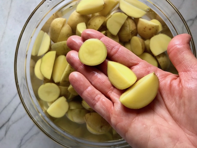 Raw Mini Gold Potatoes Cut in hand over bowl. This Flank Steak Recipe with Potatoes & Broccoli is an easy and delicious Sheet Pan Dinner. It has a flavorful rub and a tangy, light Garlic Chive Crema!