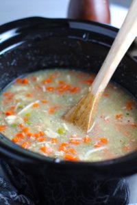 5-Ingredient Homemade Chicken Soup in a crockpot with wood spoon. This soup is thick, creamy, and hearty. It's filled with flavorful broth, meaty shredded chicken, and sweet bursts of bright veggies. You can prepare all of the ingredients ahead and freeze them until you are ready to cook. Then, thaw, pour into the Slow Cooker, set and forget.