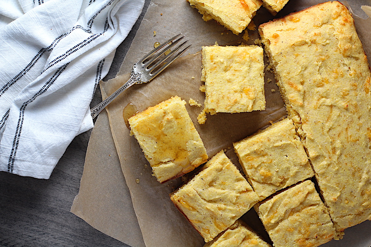 Cheddar Honey Glazed Cornbread pieces cut on parchment paper with honey drizzled on top and fork and crumbs around.