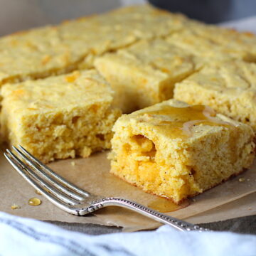 Cheddar Honey Gluten Free Cornbread pieces stacked on parchment paper with honey drizzled on top and fork and crumbs around.