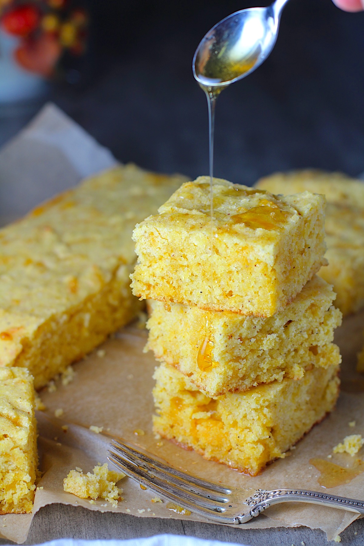 Cheddar Honey Glazed Cornbread pieces stacked on parchment paper with honey drizzled on top and fork and crumbs around.