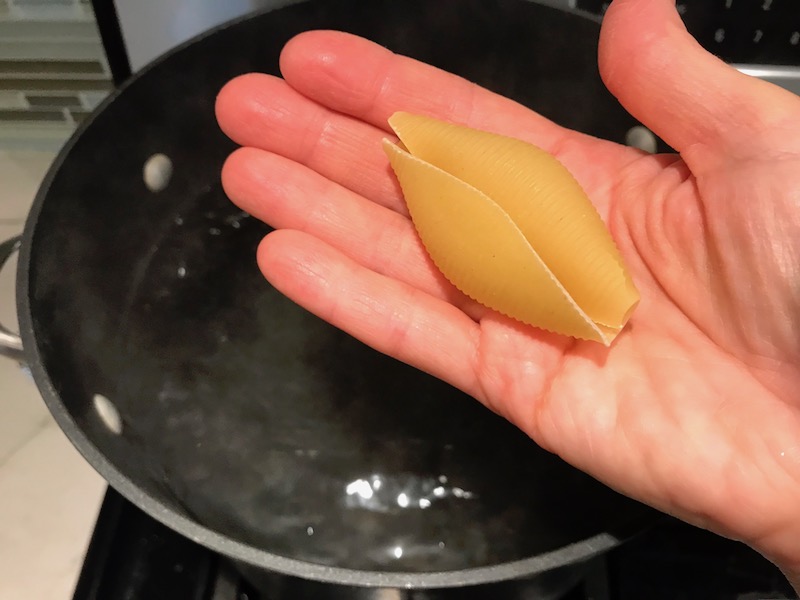 Hand holding Jumbo Pasta Shell over boiling water for Turkey Ricotta Stuffed Shells in Tomato Sauce are the perfect way to repurpose and transform leftover Turkey or Chicken. The Shredded Turkey, Italian seasonings, mozzarella, and ricotta are stuffed in shells and topped with a simple tomato sauce and more melty mozzarella and nutty parmesan, it's a perfect dish that the family will love!