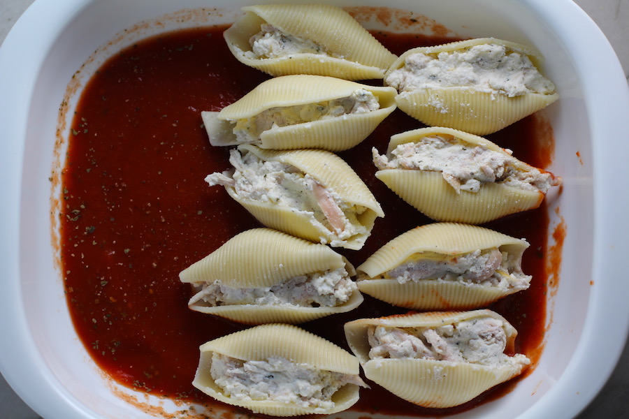 Stuffed Pasta Shells being layered into a tomato sauce in a casserole dish for Turkey Ricotta Stuffed Shells in Tomato Sauce. These are the perfect way to repurpose and transform leftover Turkey or Chicken. The Shredded Turkey, Italian seasonings, mozzarella, and ricotta are stuffed in shells and topped with a simple tomato sauce and more melty mozzarella and nutty parmesan, it's a perfect dish that the family will love!