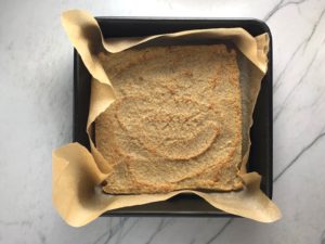 Quinoa crust baked in pan with parchment paper for the Tomato Tart Recipe. It gives you crunch from the Quinoa crust, a burst of fresh from the tomatoes, tons of flavor from the basil and garlic, tang and meatiness from the artichoke and so much creaminess from the mozzarella and goat cheese! It's addictive and delicious!