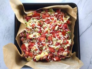Quinoa crust Tomato & Artichoke tart in pan with parchment paper for the Tomato Tart Recipe. It gives you crunch from the Quinoa crust, a burst of fresh from the tomatoes, tons of flavor from the basil and garlic, tang and meatiness from the artichoke and so much creaminess from the mozzarella and goat cheese! It's addictive and delicious!