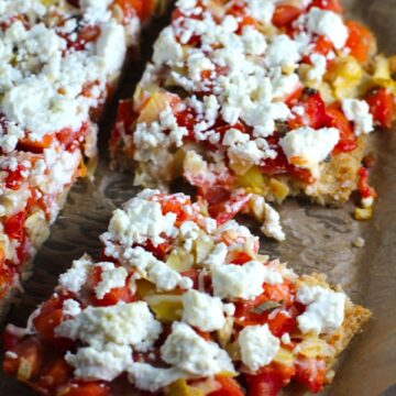 Close up of cut Tomato Tart on parchment. It gives you crunch from the Quinoa crust, a burst of fresh from the tomatoes, tons of flavor from the basil and garlic, tang and meatiness from the artichoke and so much creaminess from the mozzarella and goat cheese!  It's addictive and delicious!