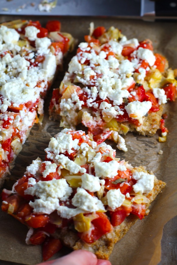 Close up of cut Tomato Tart on parchment. It gives you crunch from the Quinoa crust, a burst of fresh from the tomatoes, tons of flavor from the basil and garlic, tang and meatiness from the artichoke and so much creaminess from the mozzarella and goat cheese! It's addictive and delicious!