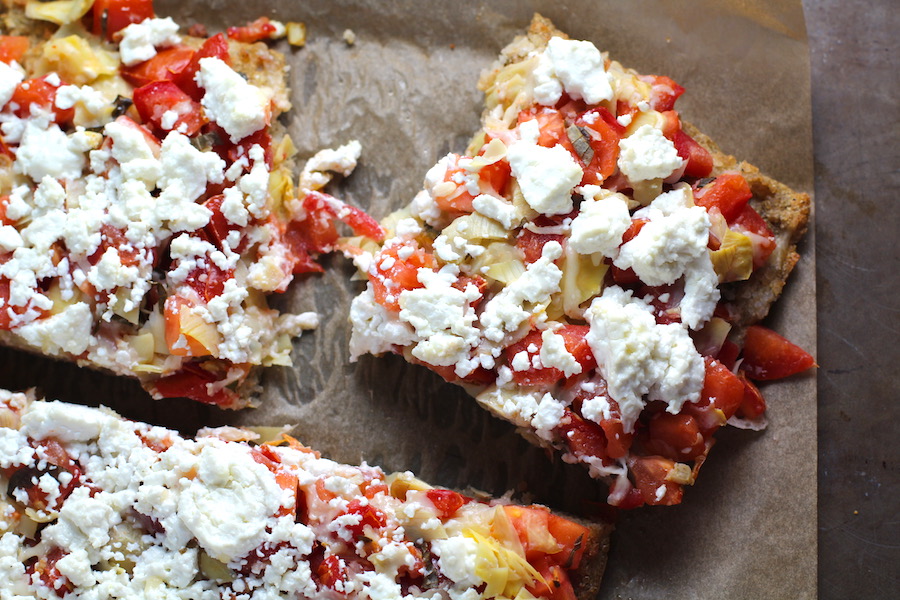 Close up of cut Tomato Tart on parchment. It gives you crunch from the Quinoa crust, a burst of fresh from the tomatoes, tons of flavor from the basil and garlic, tang and meatiness from the artichoke and so much creaminess from the mozzarella and goat cheese! It's addictive and delicious!