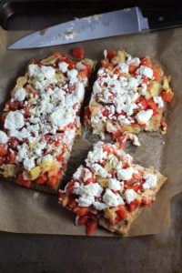 Square Tomato Tart cut into pieces on parchment. It gives you crunch from the Quinoa crust, a burst of fresh from the tomatoes, tons of flavor from the basil and garlic, tang and meatiness from the artichoke and so much creaminess from the mozzarella and goat cheese! It's addictive and delicious!