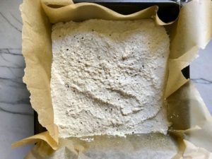 Quinoa batter in pan with parchment paper for the Tomato Tart Recipe. It gives you crunch from the Quinoa crust, a burst of fresh from the tomatoes, tons of flavor from the basil and garlic, tang and meatiness from the artichoke and so much creaminess from the mozzarella and goat cheese! It's addictive and delicious!