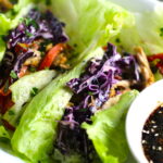 Asian Lettuce Wraps on a plate with sauce. They are a fantastic way to use leftover Turkey or Chicken transforming it with new delicious flavors and textures. The turkey is stir fried with carrots, red pepper, and brussel sprouts in a flavorful ginger, garlic, & sesame sauce. It's layered in lettuce wraps with rice and a cool, crunchy purple cabbage sesame slaw. Serve with a Garlic Honey Soy Sauce....YUM!!!