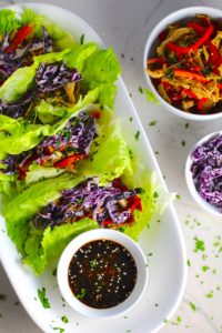 Asian Lettuce Wraps on a plate with sauce. They are a fantastic way to use leftover Turkey or Chicken transforming it with new delicious flavors and textures. The turkey is stir fried with carrots, red pepper, and brussel sprouts in a flavorful ginger, garlic, & sesame sauce. It's layered in lettuce wraps with rice and a cool, crunchy purple cabbage sesame slaw. Serve with a Garlic Honey Soy Sauce....YUM!!!