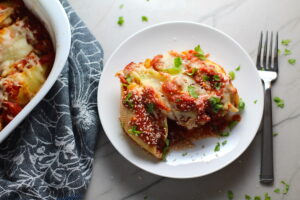leftover turkey pasta bake Stuffed Shells in Tomato Sauce on plate with casserole dish in background. These are the perfect way to repurpose and transform leftover Turkey or Chicken. The Shredded Turkey, Italian seasonings, mozzarella, and ricotta are stuffed in shells and topped with a simple tomato sauce and more melty mozzarella and nutty parmesan, it's a perfect dish that the family will love!