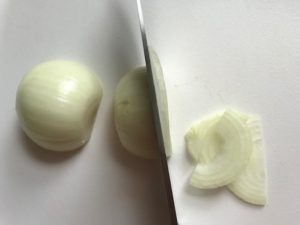 Knife starting to slice onions on cutting board for the Caramelized Onions & Mushrooms on Pork Tenderloin recipe. This is such a flavorful main dish! The pork tenderloin is moist and juicy and topped with Onions & Mushrooms that are sauteed low and slow with a touch of balsamic to bring out all of the natural sugars and caramelize them to perfection.