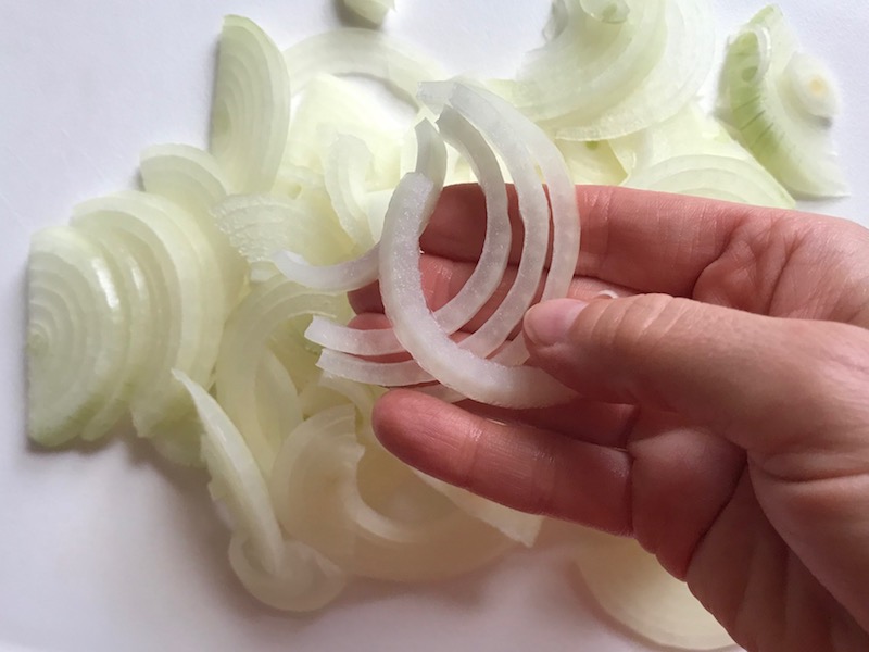 Sliced onions in hand and on cutting board for the Caramelized Onions & Mushrooms on Pork Tenderloin recipe. This is such a flavorful main dish! The pork tenderloin is moist and juicy and topped with Onions & Mushrooms that are sauteed low and slow with a touch of balsamic to bring out all of the natural sugars and caramelize them to perfection.