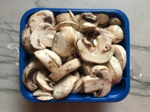 Sliced raw mushrooms in carton for the Caramelized Onions & Mushrooms on Pork Tenderloin recipe. This is such a flavorful main dish! The pork tenderloin is moist and juicy and topped with Onions & Mushrooms that are sauteed low and slow with a touch of balsamic to bring out all of the natural sugars and caramelize them to perfection.