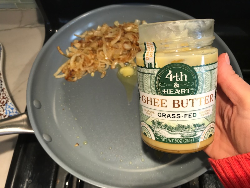 Sliced onions cooking in skillet and pushed to side as ghee is added for the Caramelized Onions & Mushrooms on Pork Tenderloin recipe. This is such a flavorful main dish! The pork tenderloin is moist and juicy and topped with Onions & Mushrooms that are sauteed low and slow with a touch of balsamic to bring out all of the natural sugars and caramelize them to perfection.